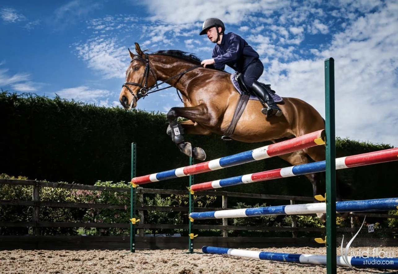 Equestrian rider and horse clearing a show-jumping obstacle beneath a blue sky