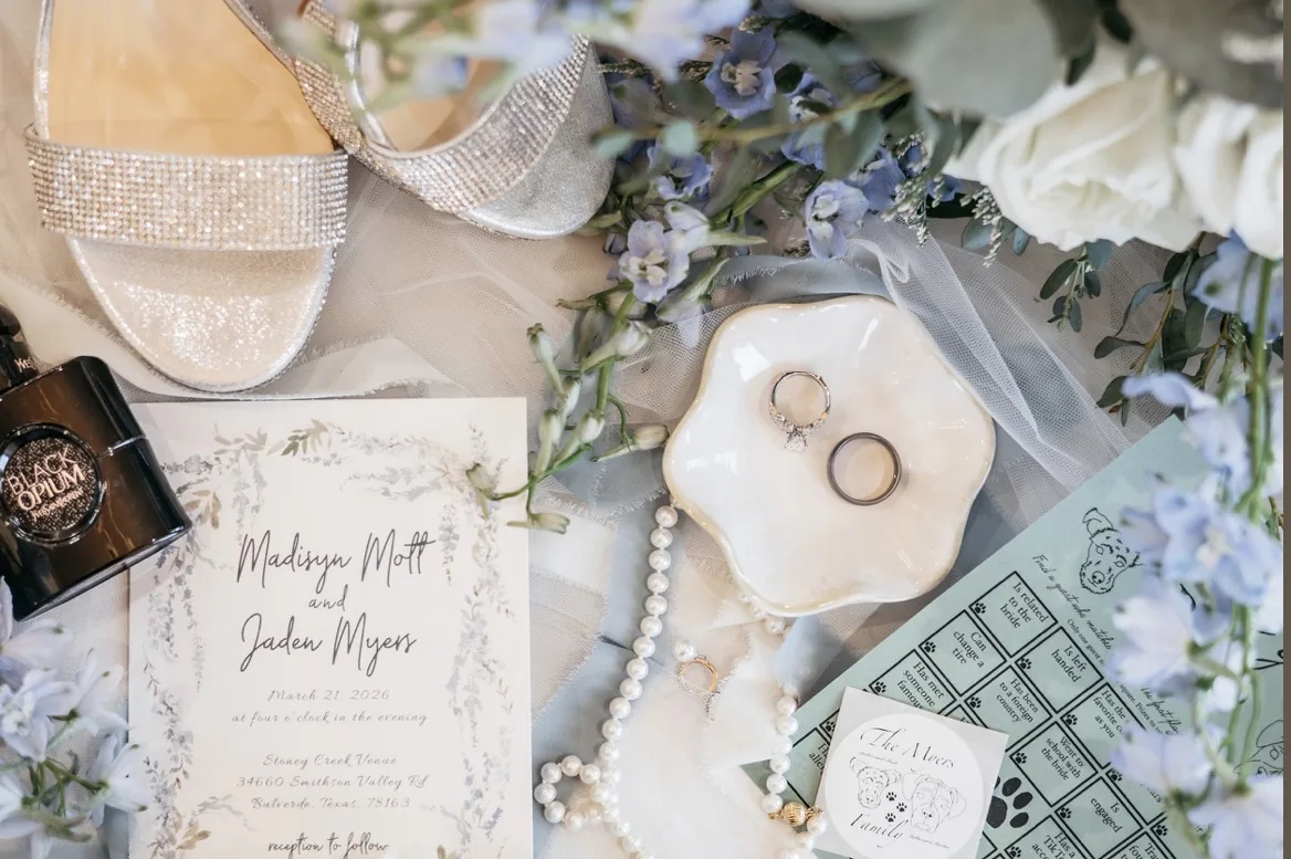 Bridal flat lay with wedding rings, invitation suite, sparkling heels and blue florals