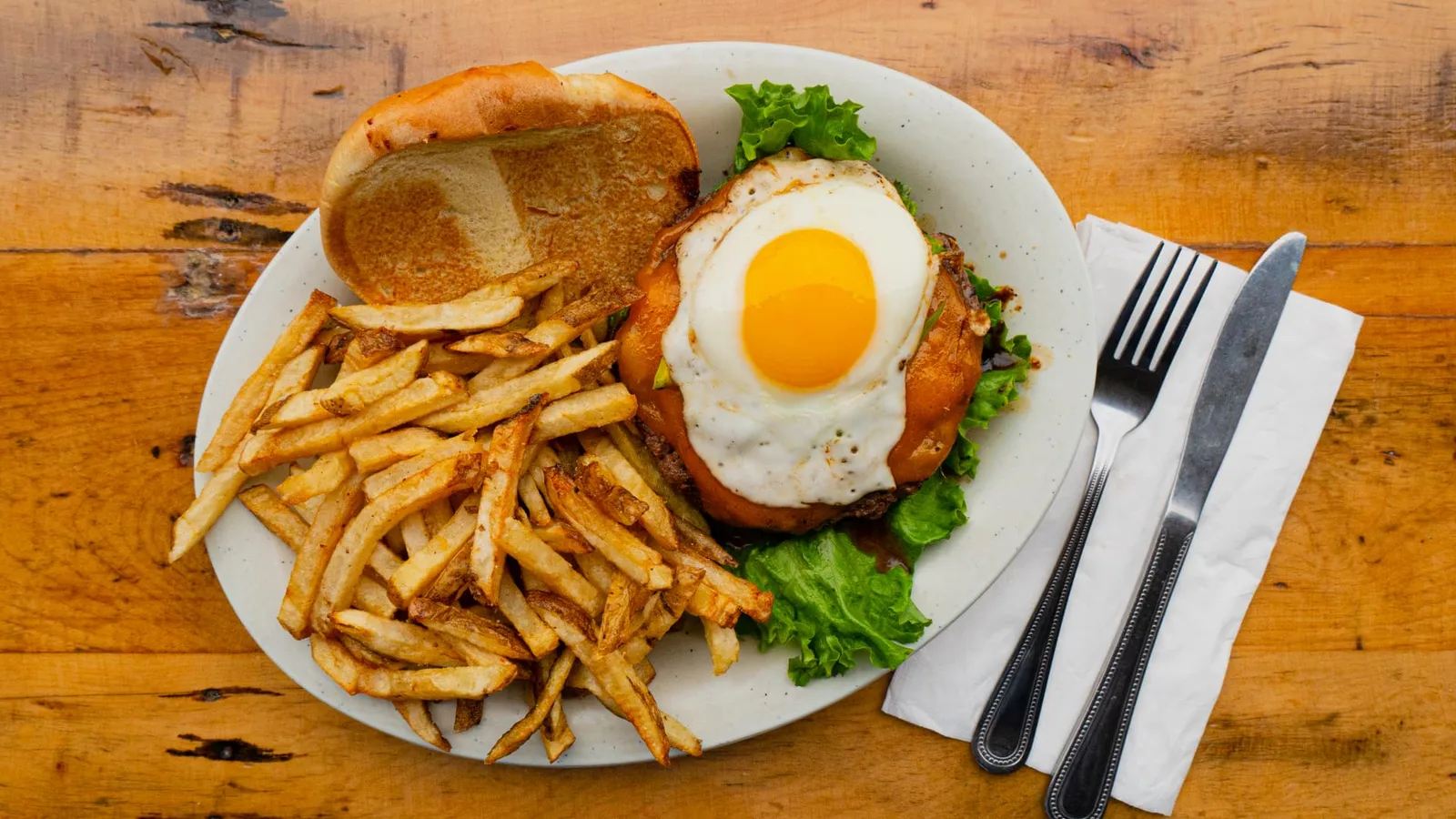 Restaurant photograph of a burger topped with a fried egg served with hand-cut fries, photographed by John, a Brand With Care creative partner