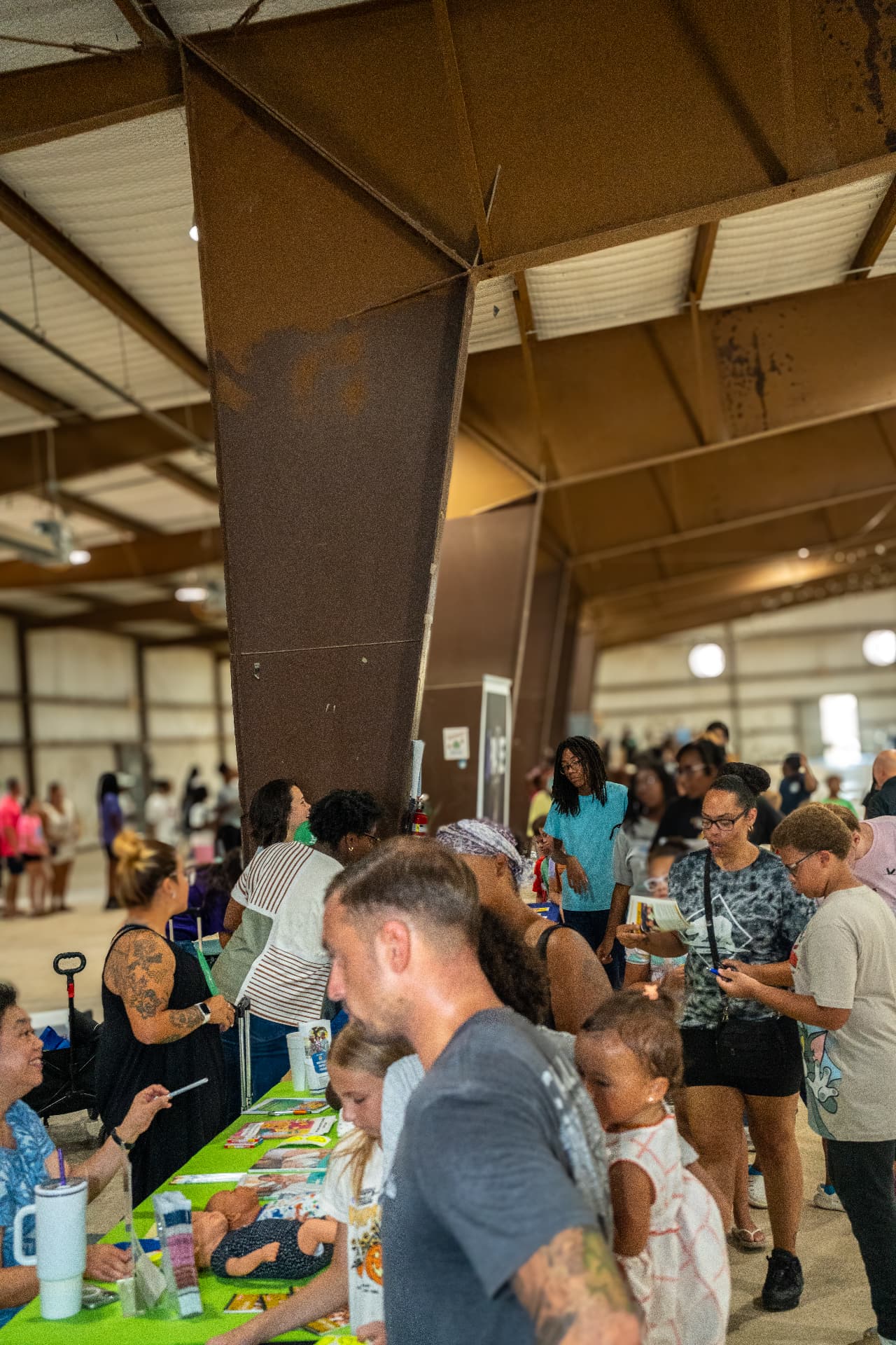 Attendees browsing exhibitor tables at a busy community event, photographed by IVAN
