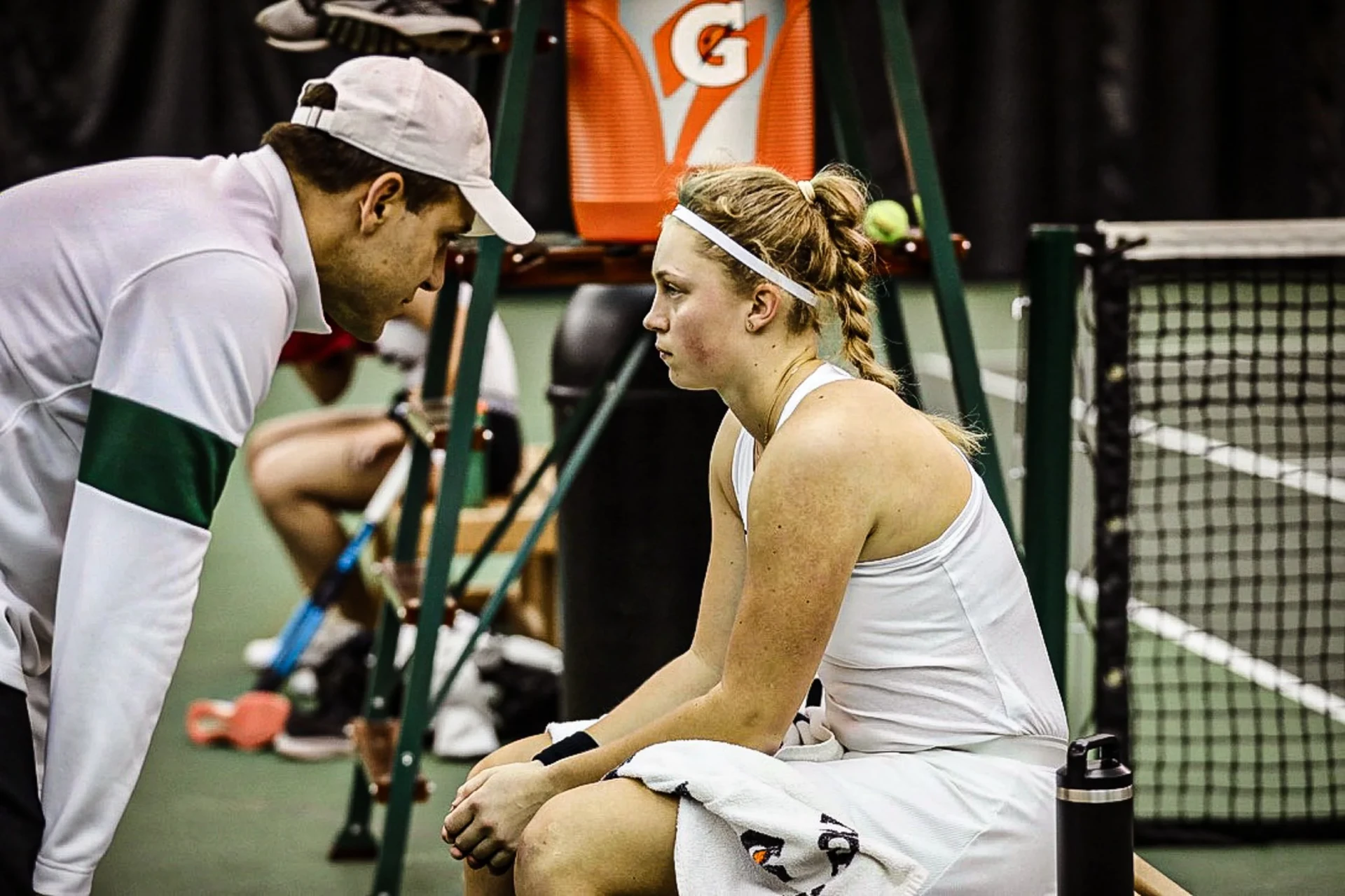 Tennis coach speaking with a seated player during an indoor match