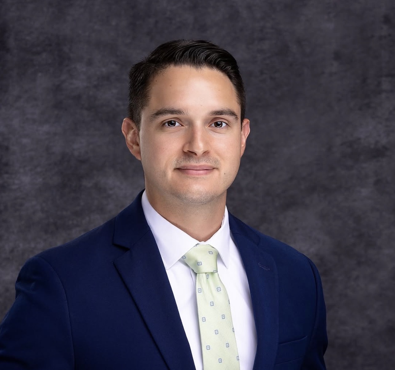Corporate headshot of a man in a navy suit and light green tie