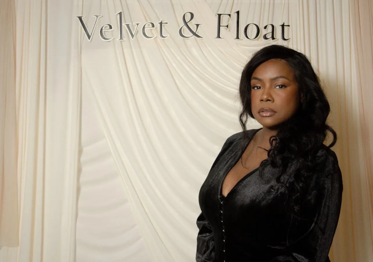 Brand portrait of a woman in a black velvet dress standing beside a cream draped backdrop