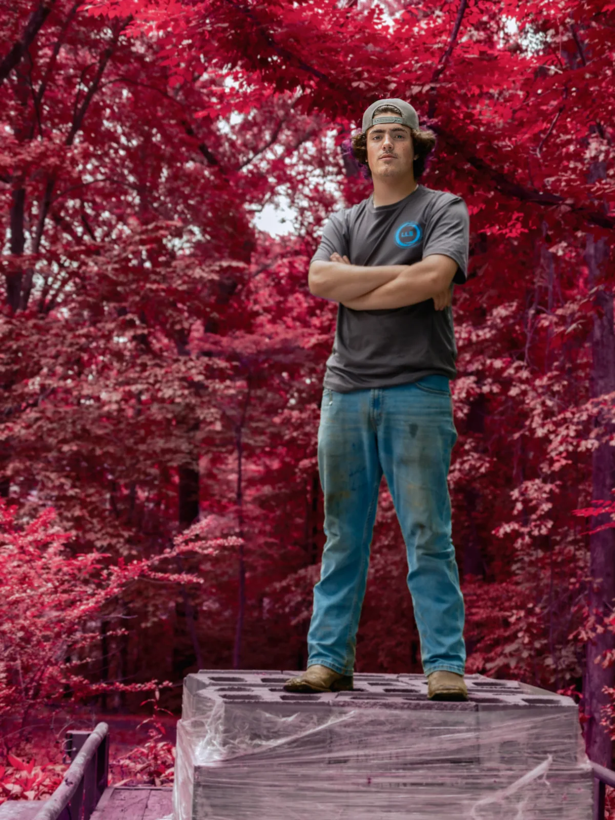 Outdoor branded portrait of a worker standing on stacked blocks beneath vivid red foliage, photographed by John, a Brand With Care creative partner