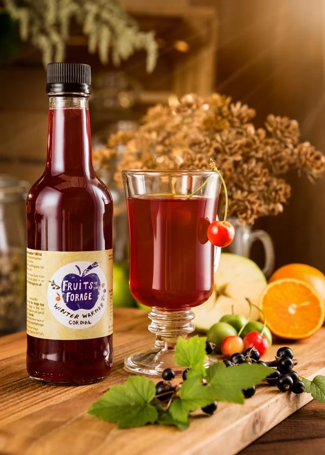 Winter berry cordial bottle and warm drink styled with fresh fruit and foliage