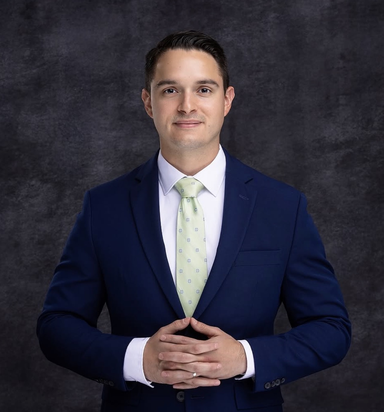 Professional headshot of a man in a navy suit with hands clasped