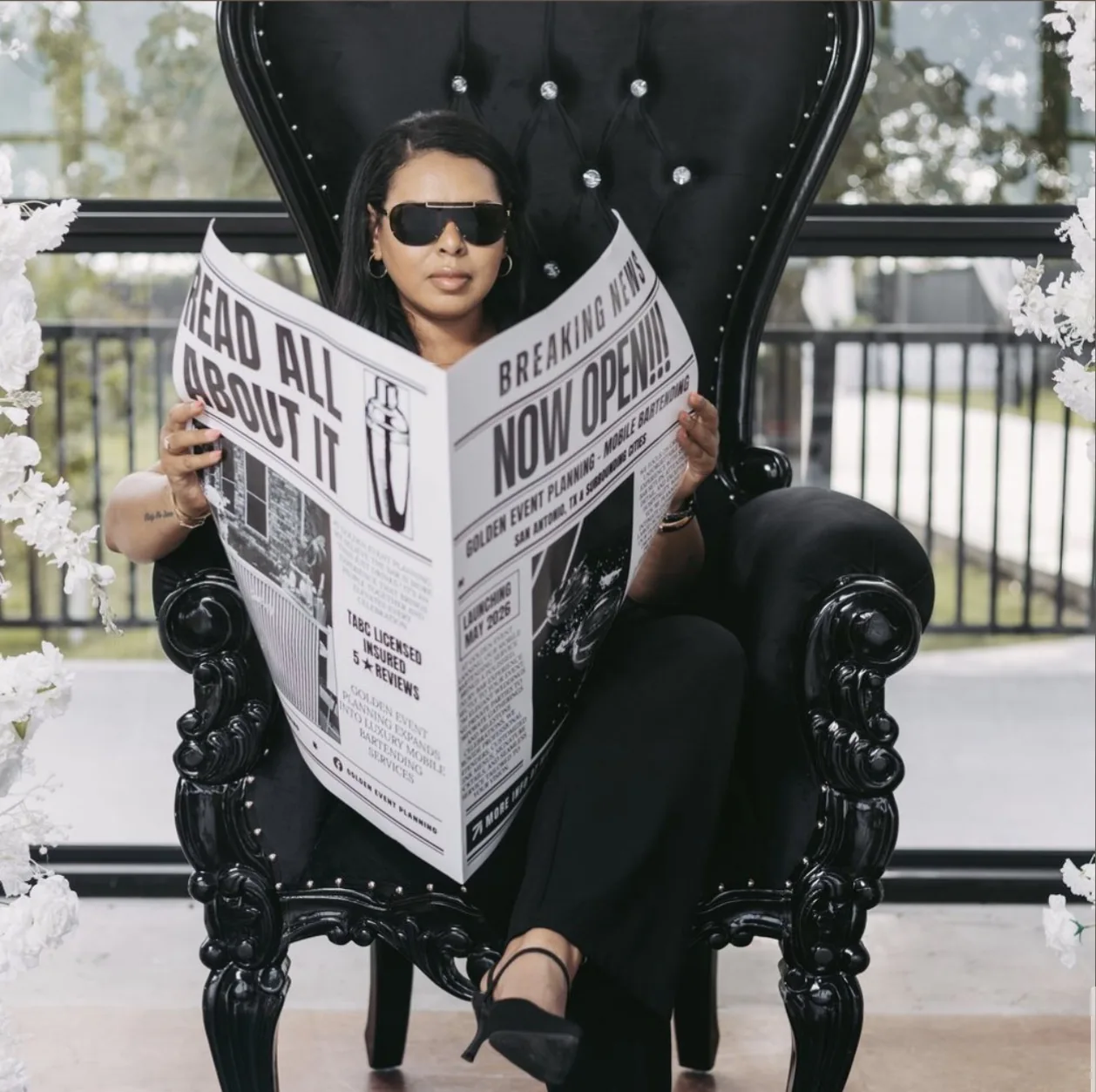 Editorial branding portrait of a business owner seated in a black throne chair reading a custom newspaper