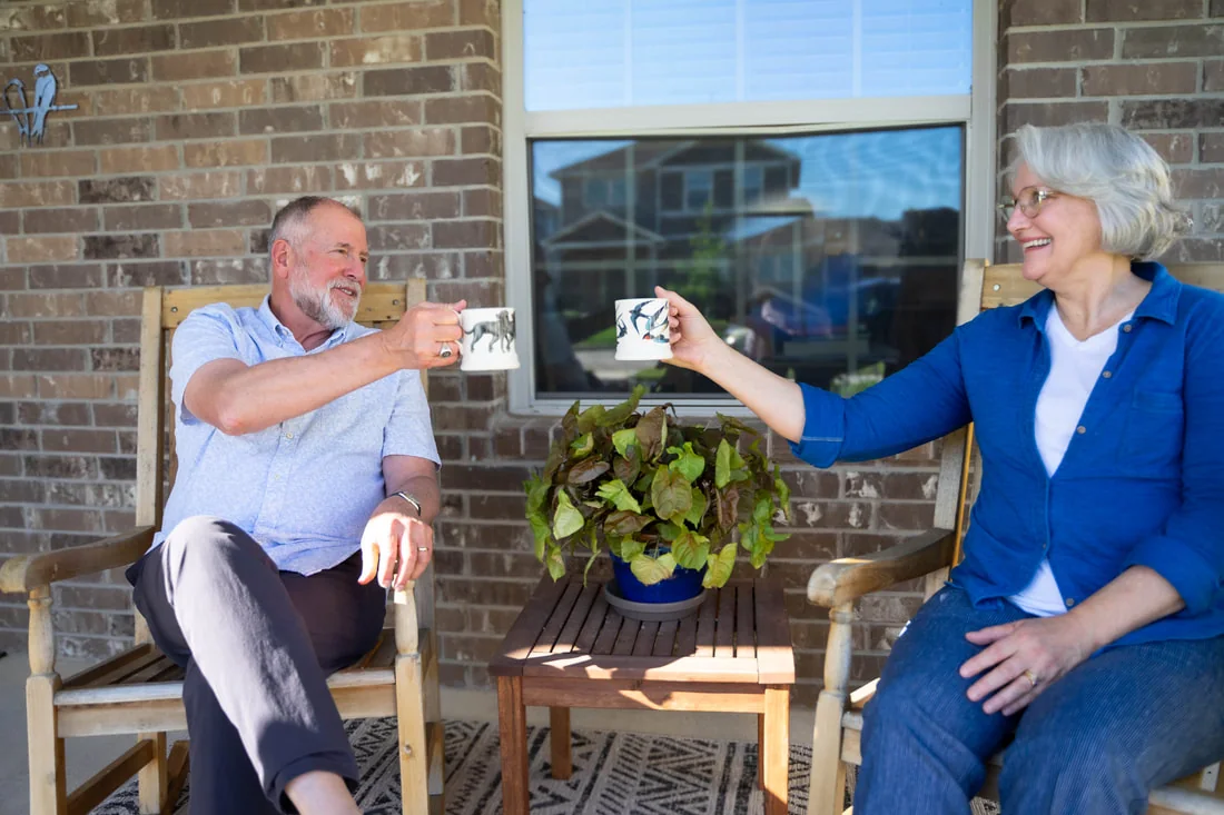 Smiling couple sharing coffee while seated on a sunny front porch