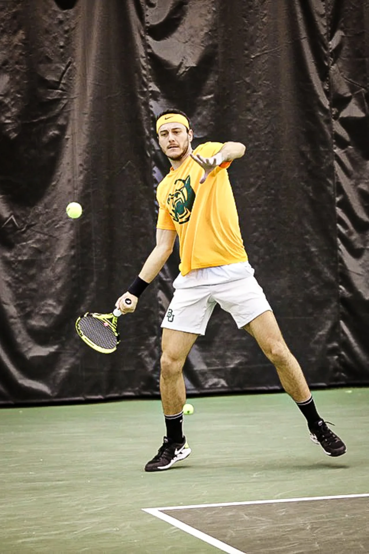 Collegiate tennis player hitting a forehand on an indoor court
