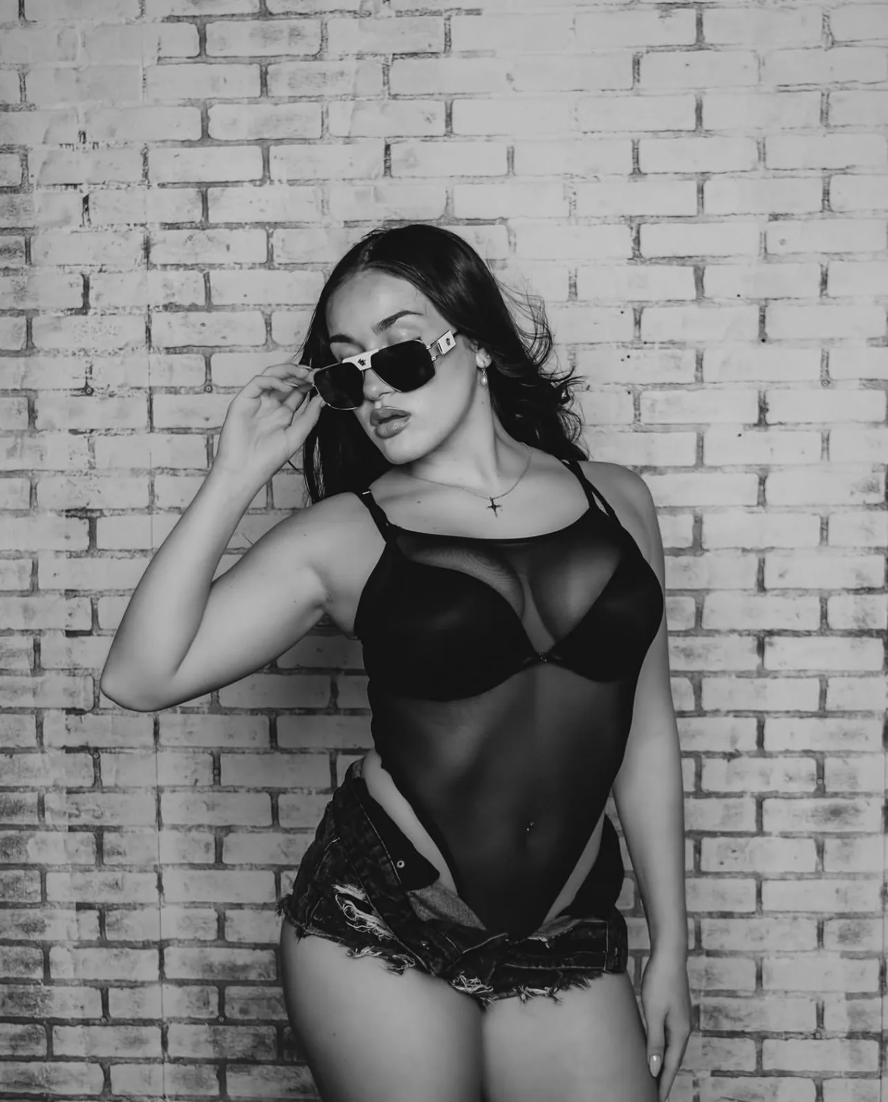 Black and white fashion portrait of a woman in sunglasses posing against a painted brick wall