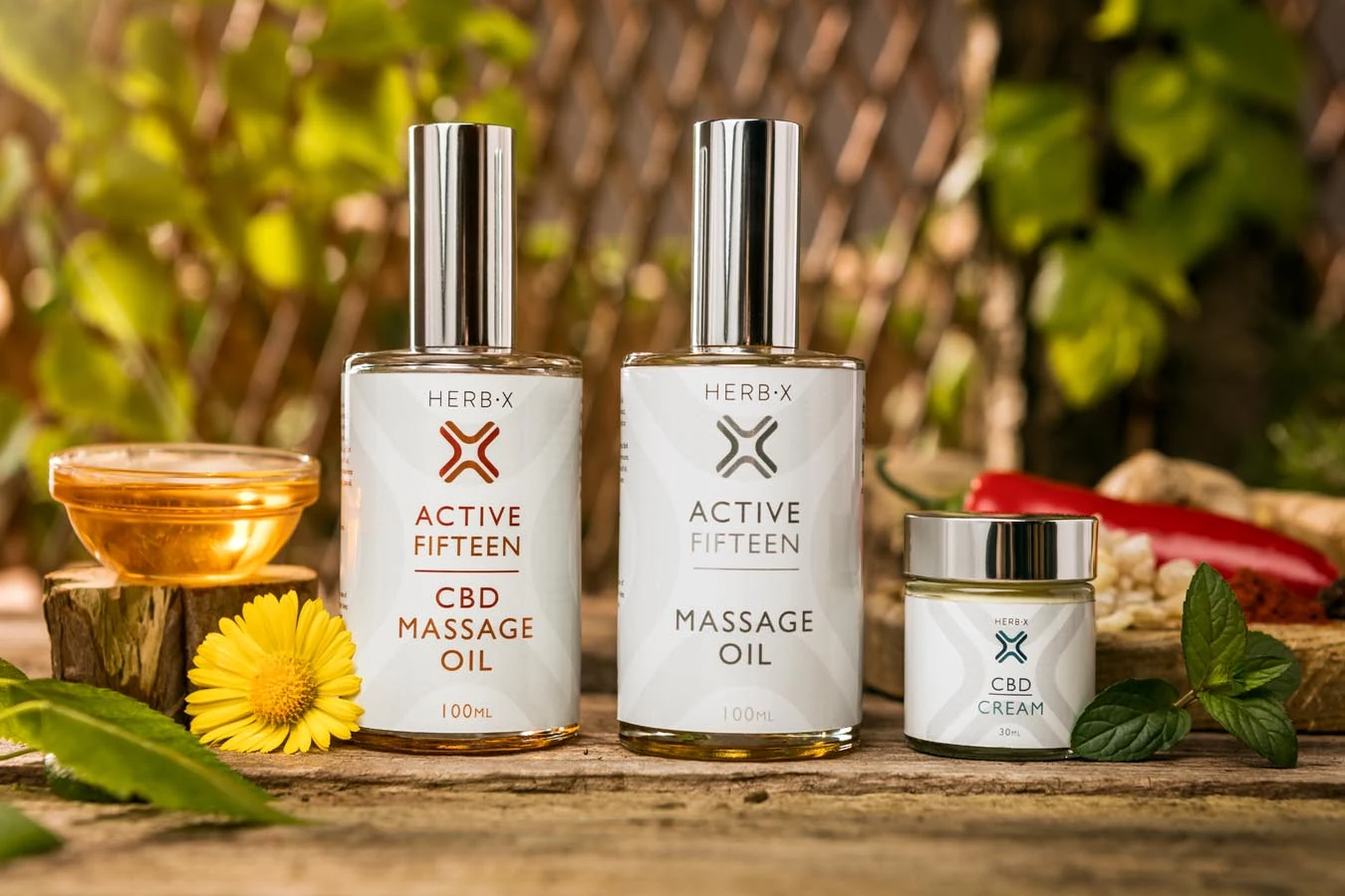 Massage oil and cream products arranged outdoors with herbs, flowers and natural ingredients