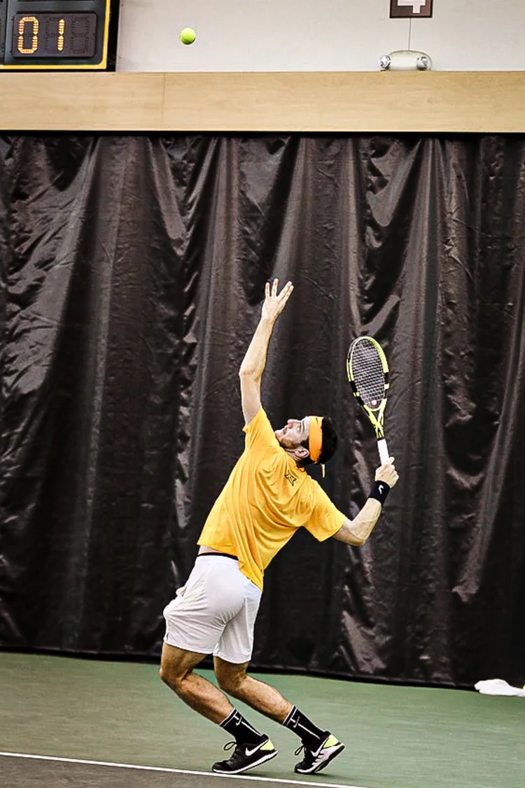 Tennis player reaching up to serve during an indoor match