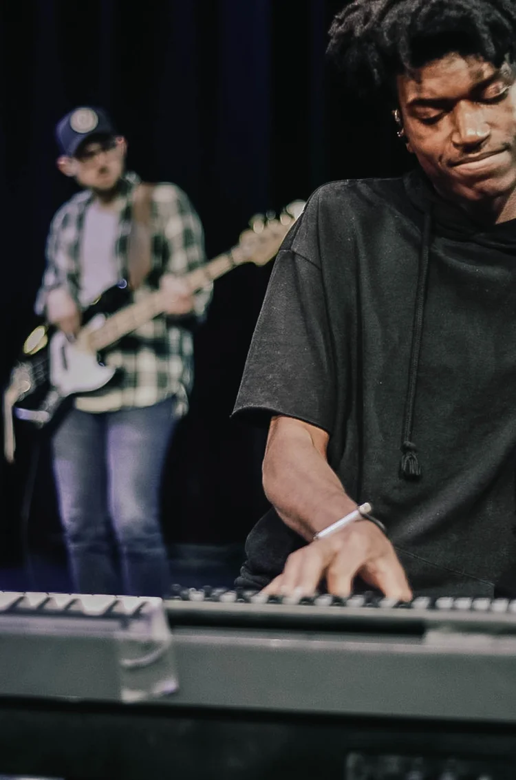 Keyboard player performing on stage with a bass guitarist behind him