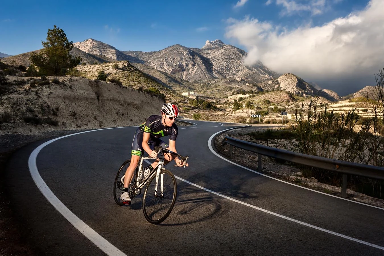 Road cyclist riding through a winding mountain landscape beneath dramatic clouds