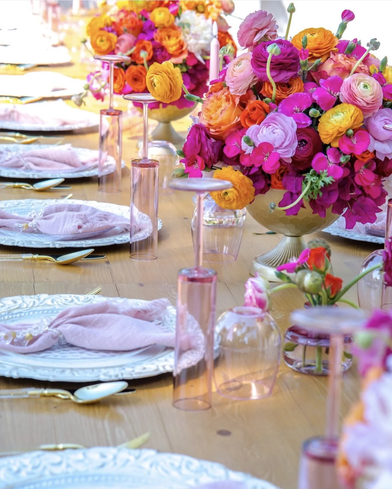 Event tablescape with pink and orange floral centerpieces, blush napkins and gold flatware on a wooden table