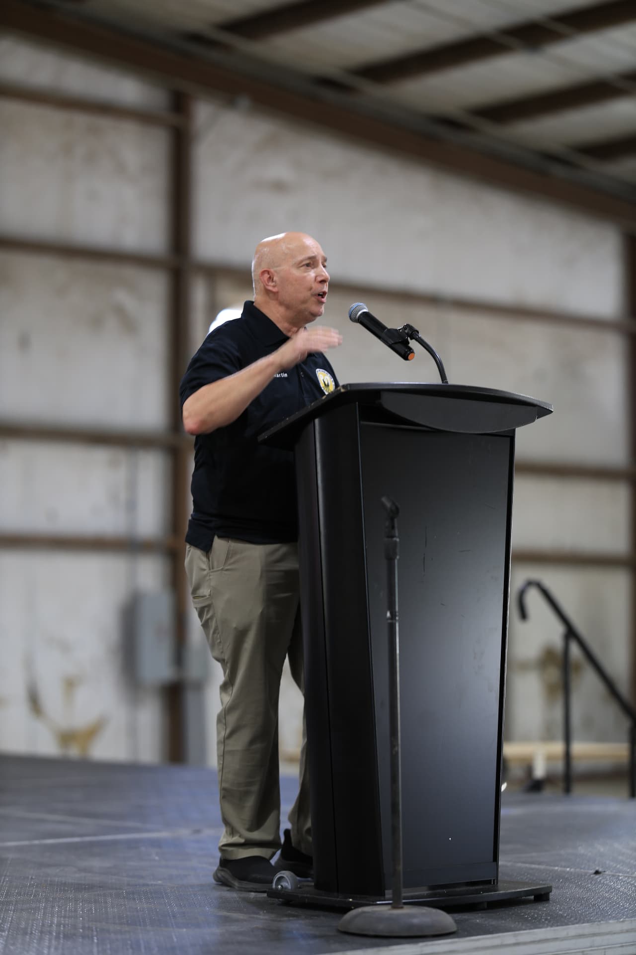 Speaker addressing the crowd from a podium at a community event, photographed by IVAN