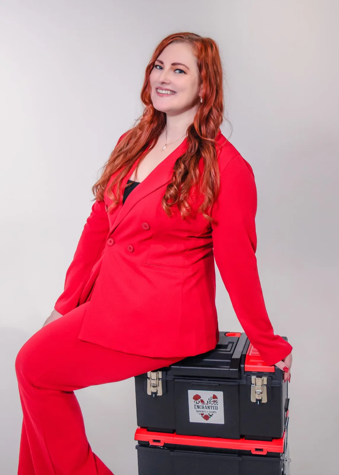 Studio branding portrait of a woman in a red suit seated on stacked equipment cases