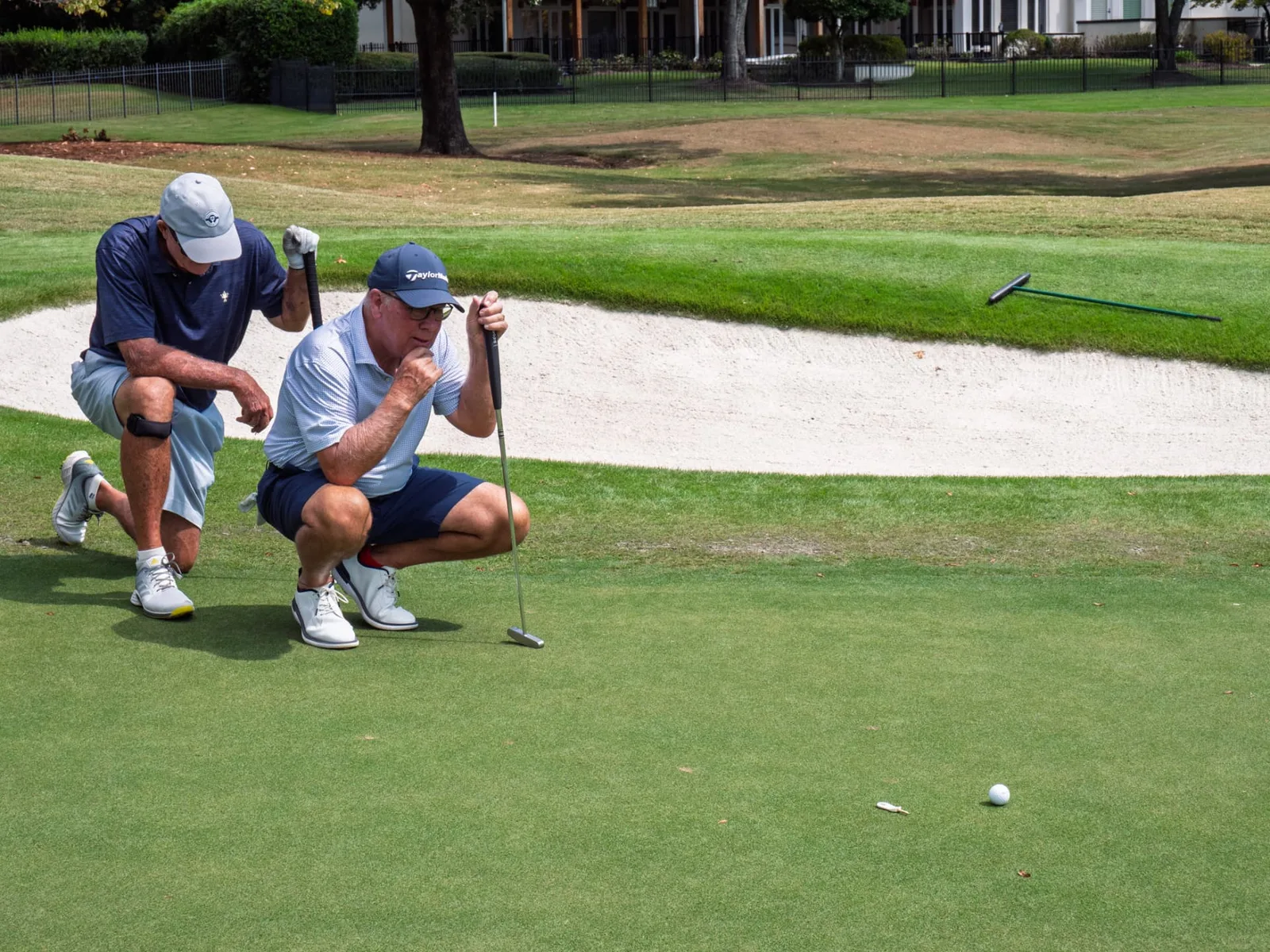 Two golfers reading a putt on a sunlit green during a charity tournament, photographed by John, a Brand With Care creative partner