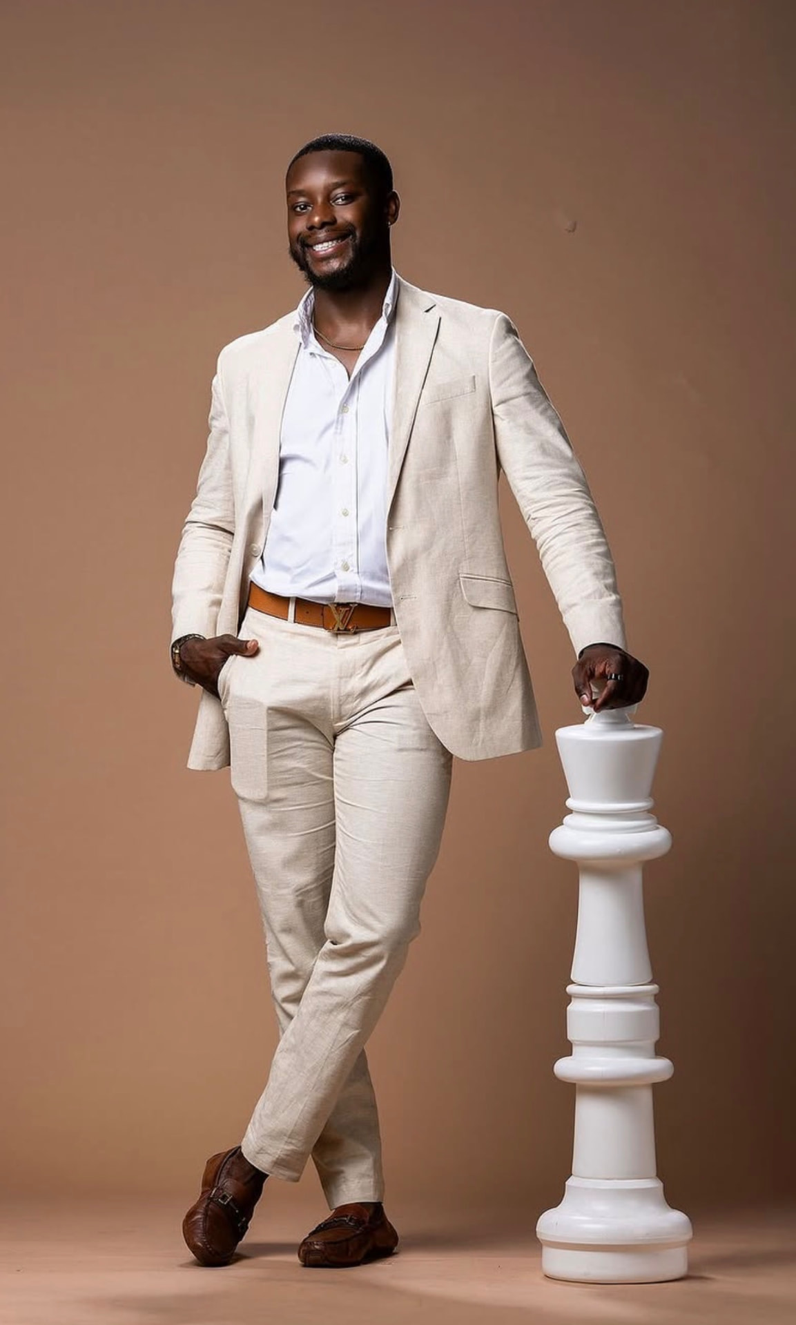 Full-length studio portrait of a man in a linen suit beside a chess king