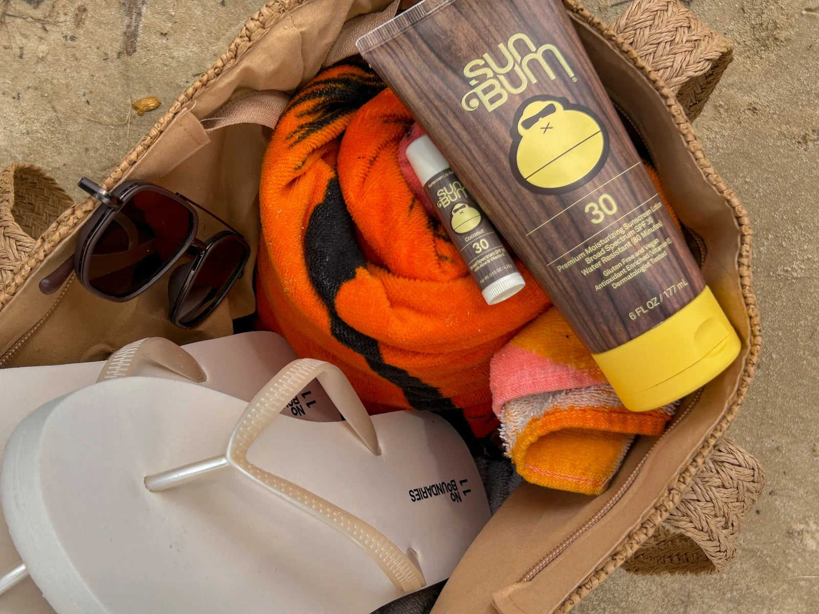 Sunscreen and beach accessories arranged in a woven bag photographed by Lindsey