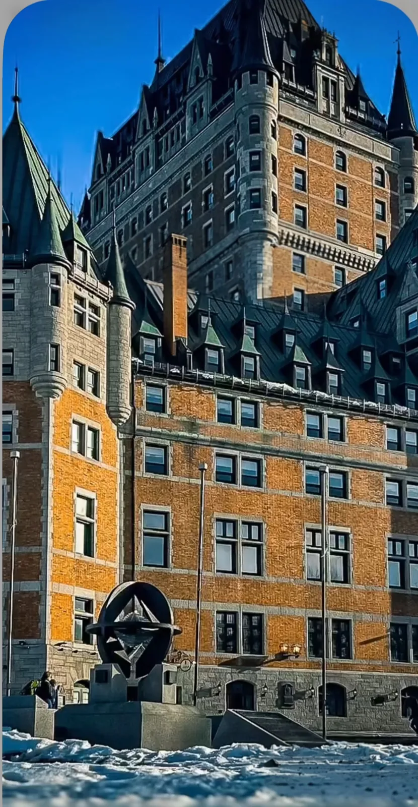 Historic stone and brick chateau-style hotel with steep green roofs under a clear blue winter sky