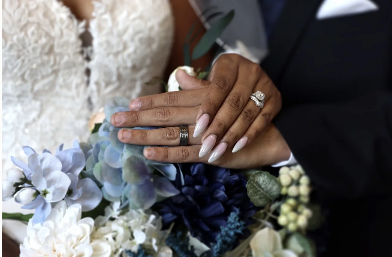 Close-up of a newlywed couple's hands and wedding rings resting on a blue and white bouquet