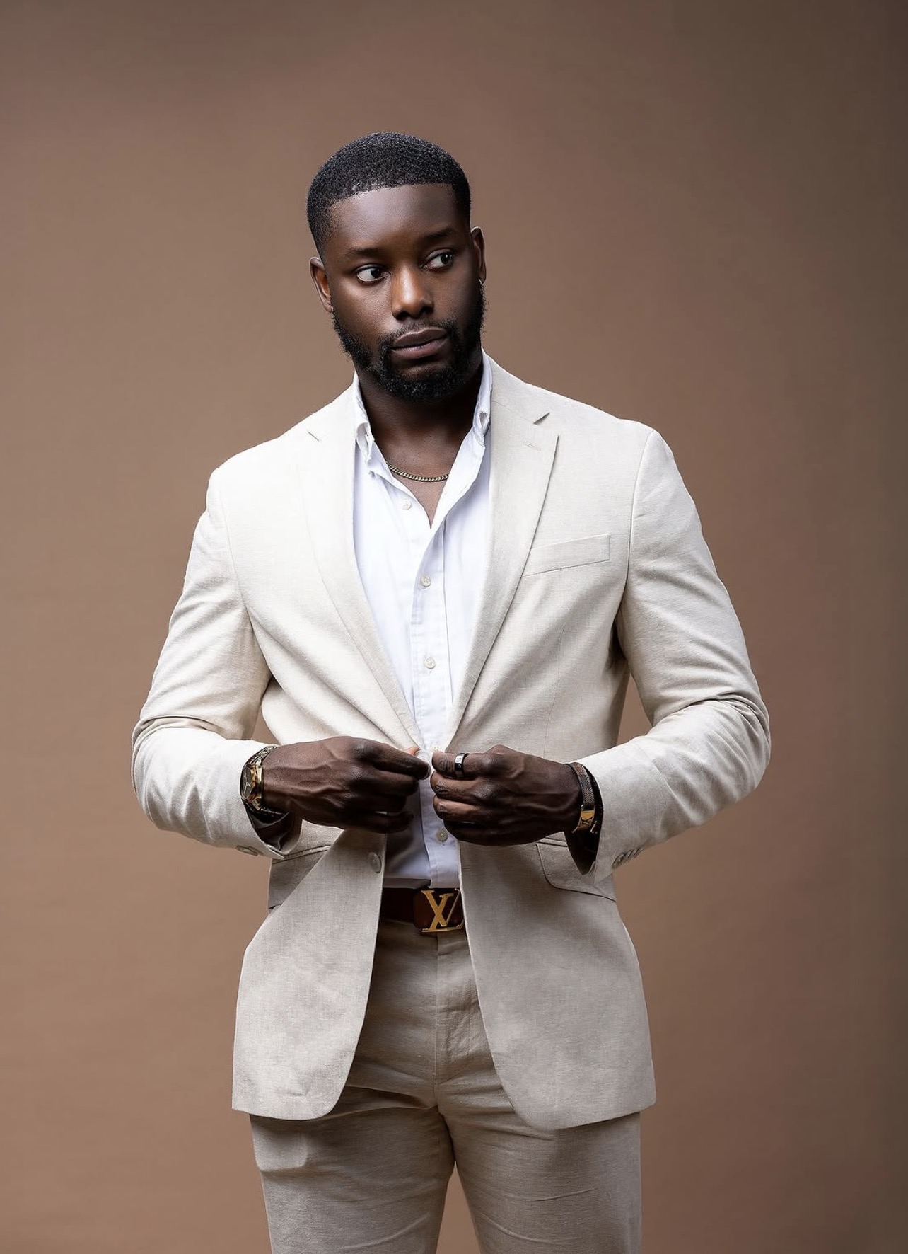 Studio portrait of a man in a cream linen suit buttoning his jacket