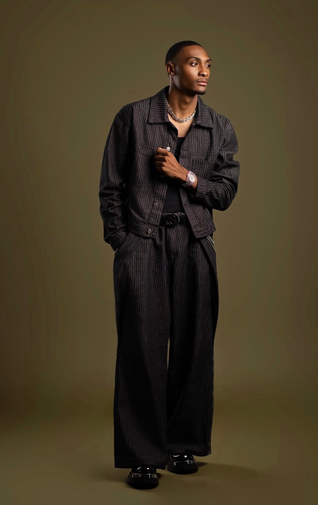 Full-length studio portrait of a man in a pinstripe set on an olive backdrop