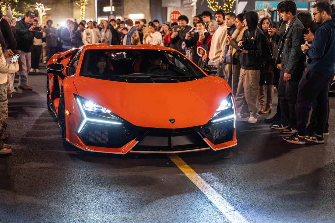Orange sports car arriving before a crowd at an evening automotive event