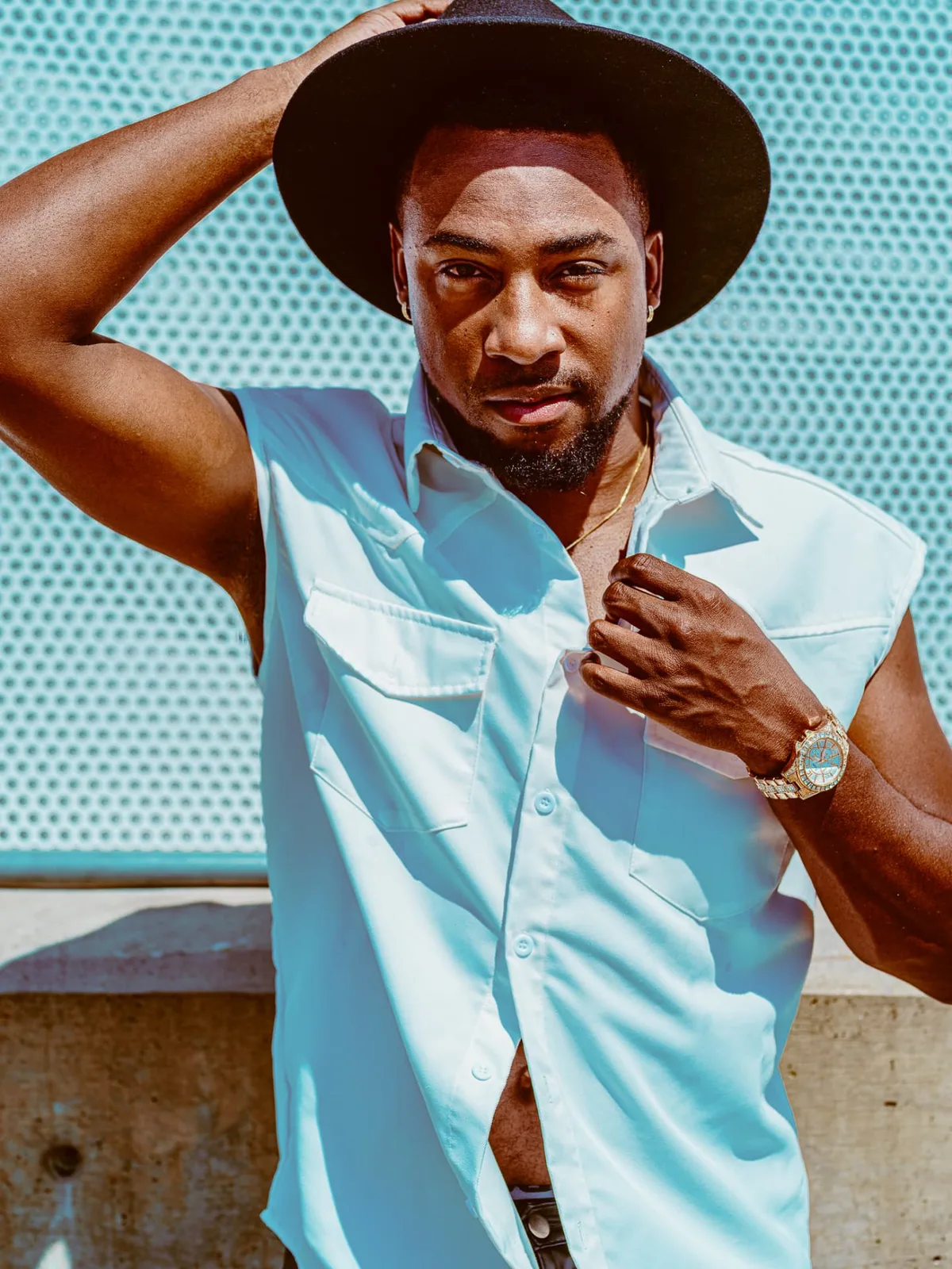 Editorial portrait of a man in a light sleeveless shirt and wide-brim hat against a teal wall, photographed by John, a Brand With Care creative partner