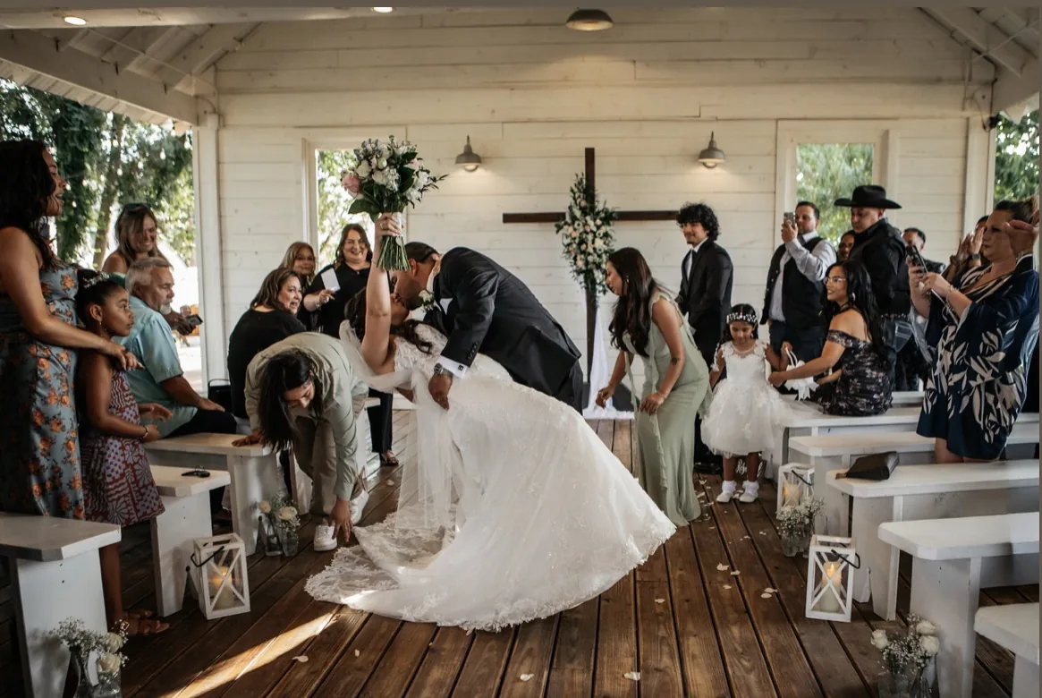Ceremony kiss in a white wooden chapel with the bride raising her bouquet