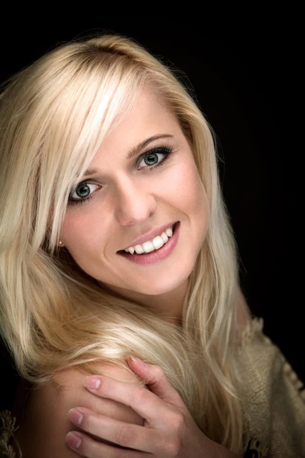 Studio beauty portrait of a smiling blonde woman against a black background