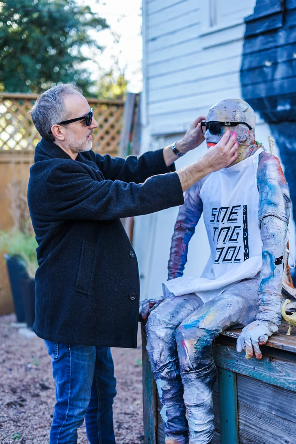 Artist placing sunglasses on a colorful seated sculpture outdoors