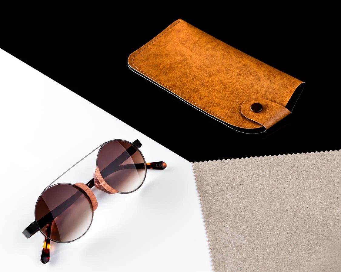Studio product flat lay of sunglasses, a leather case and a cleaning cloth