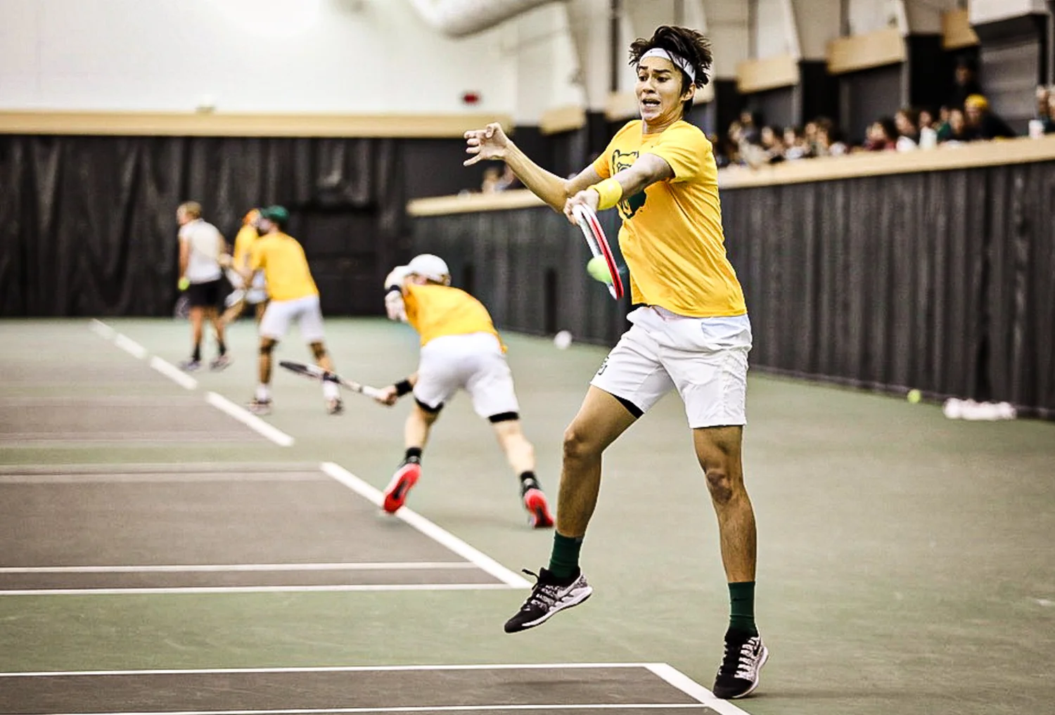Tennis player leaping to hit a forehand during indoor doubles play