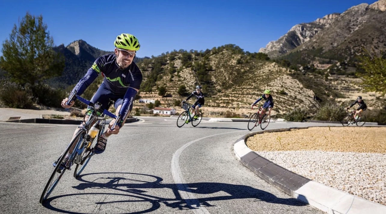 Group of road cyclists navigating a mountain bend beneath a clear blue sky